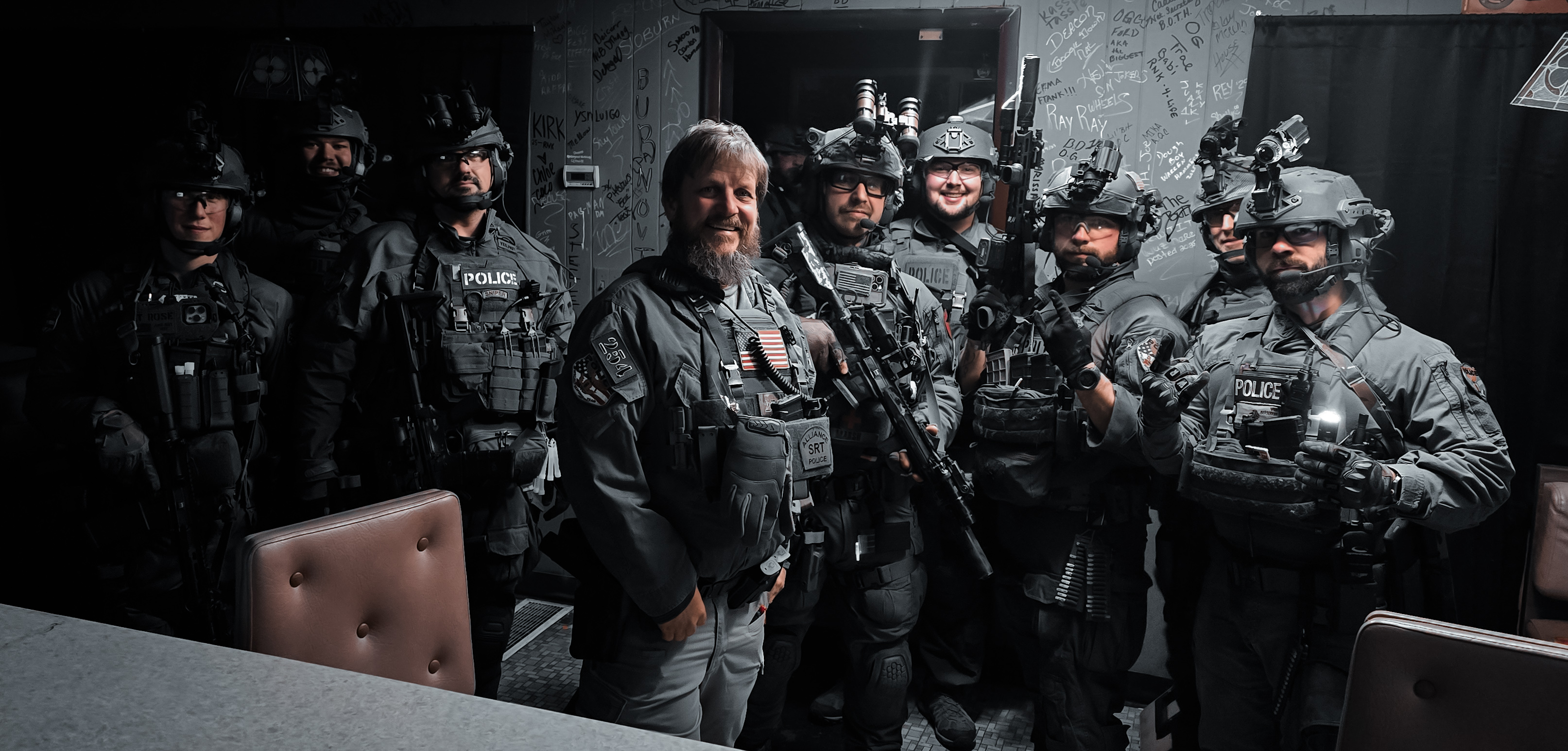 Group of armed police officers in tactical gear posing indoors with serious expressions.