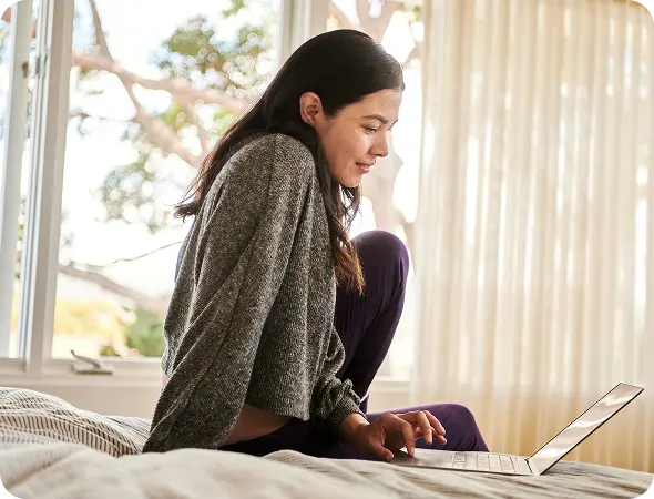 Young woman in bed researching on laptop.