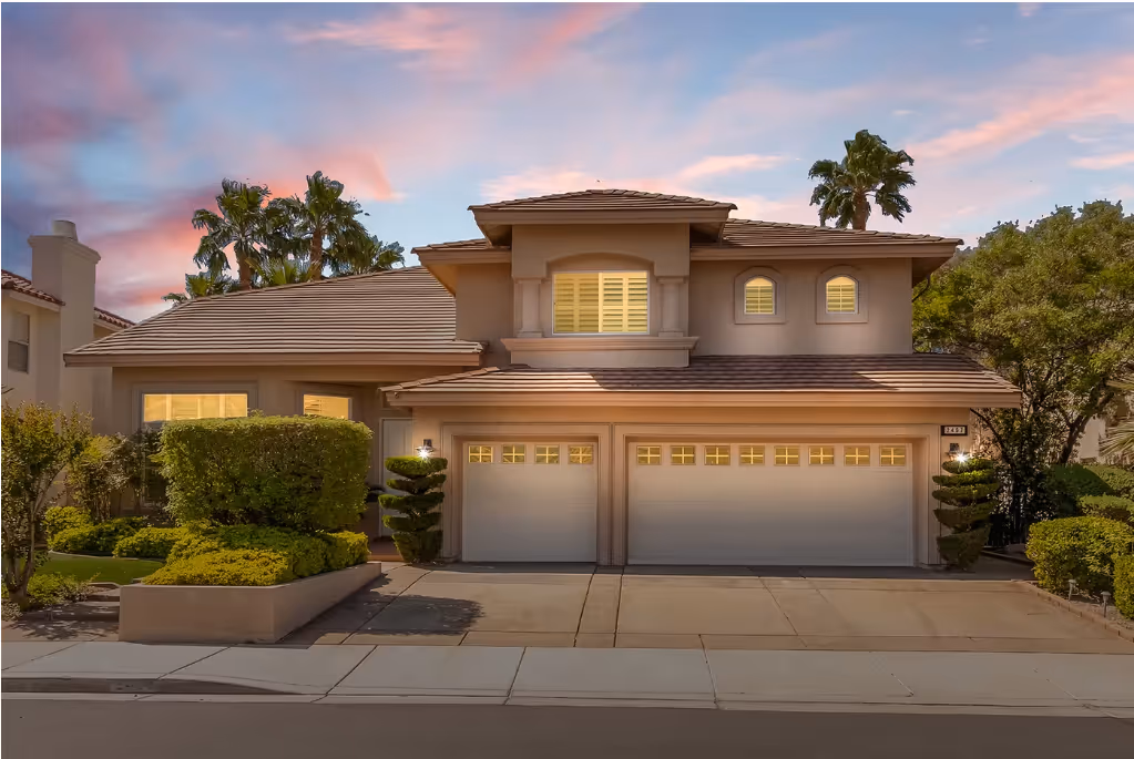 Elegant two-story suburban home with three-car garage, manicured landscaping, and warm sunset sky backdrop.