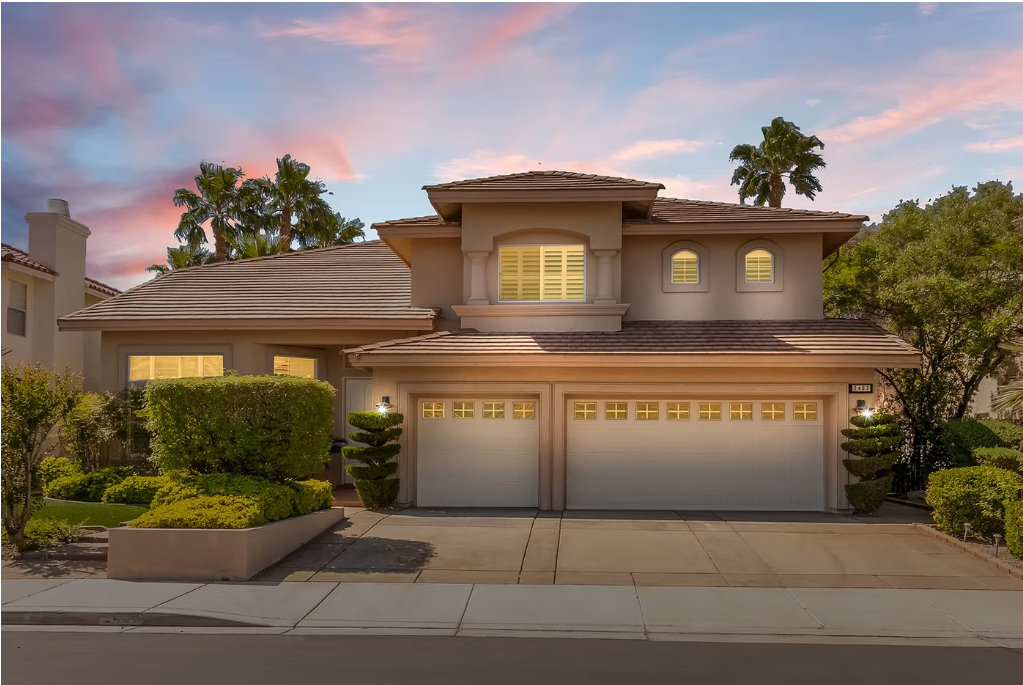 Elegant two-story suburban home with three-car garage, manicured landscaping, and warm sunset sky backdrop.