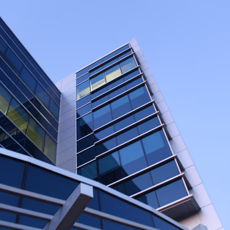 Low-angle view of a modern glass office building with reflective blue windows and a clear sky background.