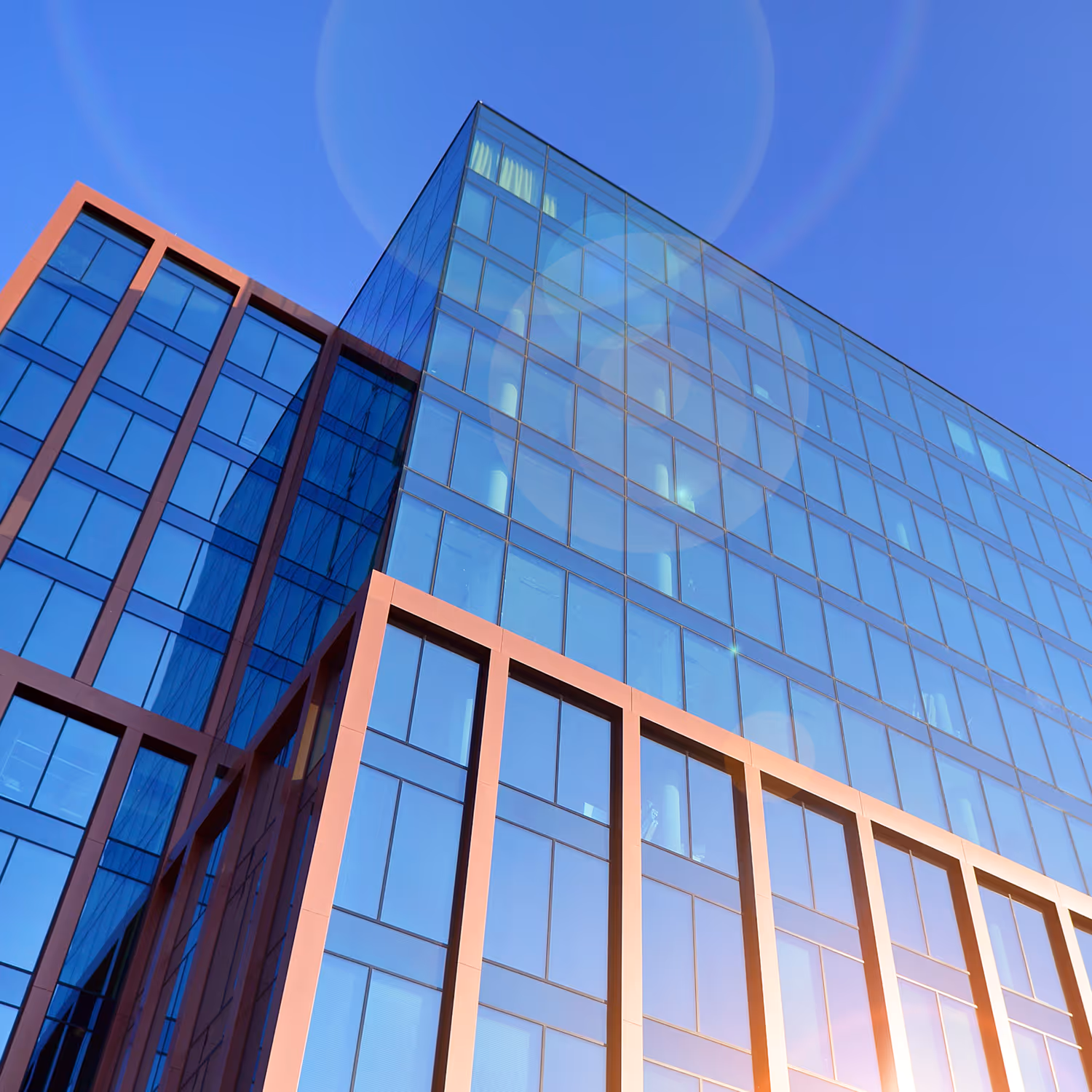 Modern glass office building with sunlight reflections under a clear blue sky.