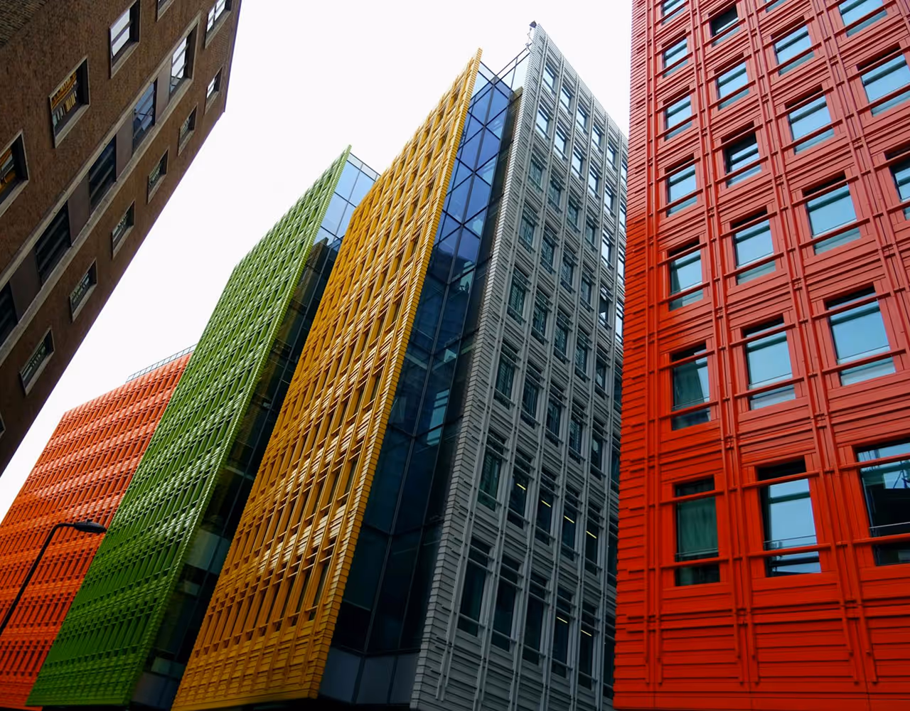 Upward view of modern city buildings with bright red, gray, yellow, green, and orange facades and patterned window designs.