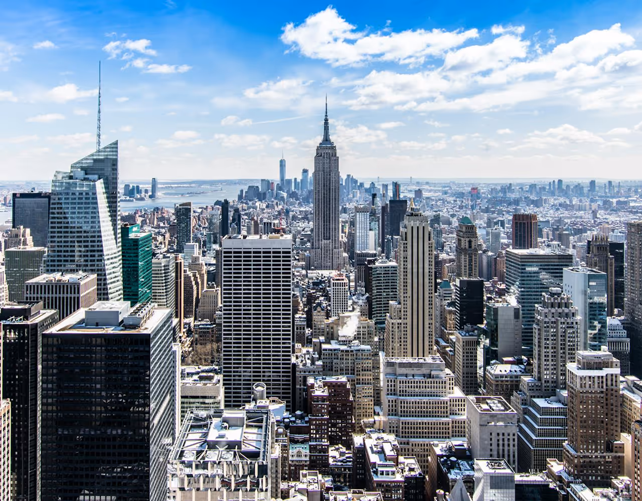 Panoramic view of New York City skyline featuring the Empire State Building under a partly cloudy sky.