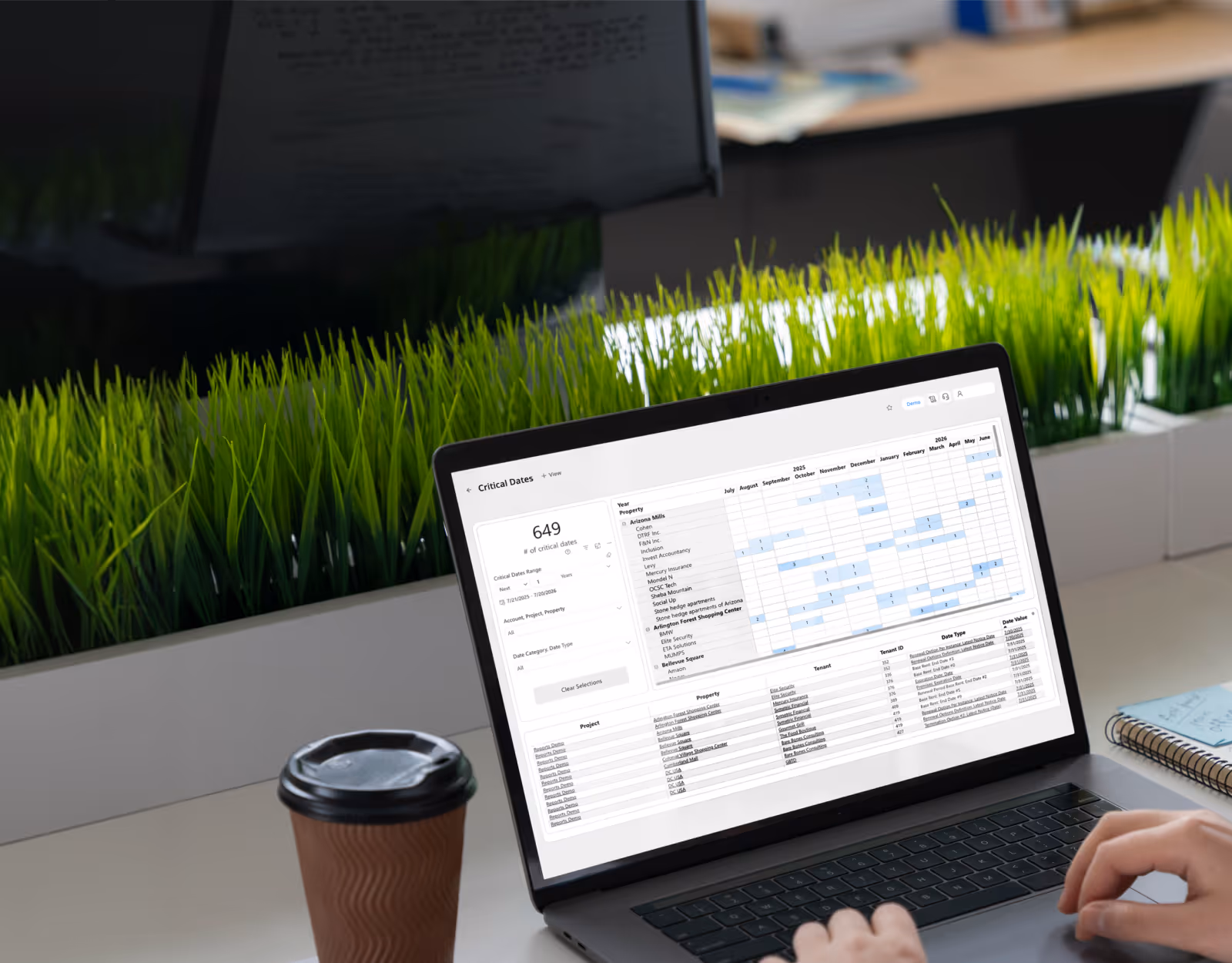 Person using a laptop displaying a Dealsumm dashboard with critical dates calendar and property project list, with a coffee cup and notebook on the desk.