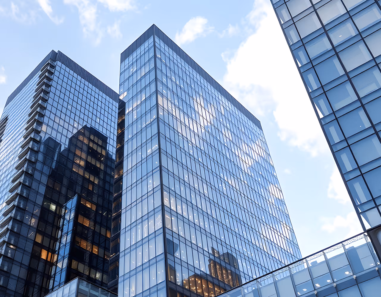 Modern glass skyscrapers reflecting a partly cloudy blue sky.