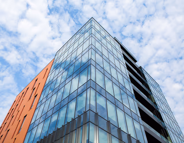 Modern glass and brick building with reflective windows under a partly cloudy sky.