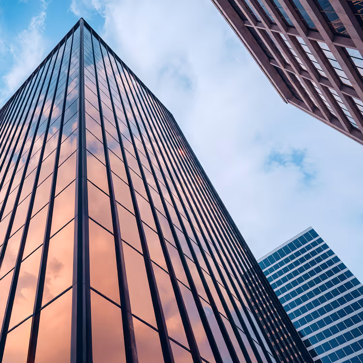 Low-angle view of glass skyscrapers reflecting a pink sky with clouds.