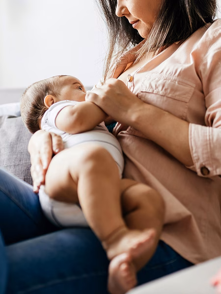 Woman in jeans and pink top breastfeeding a baby