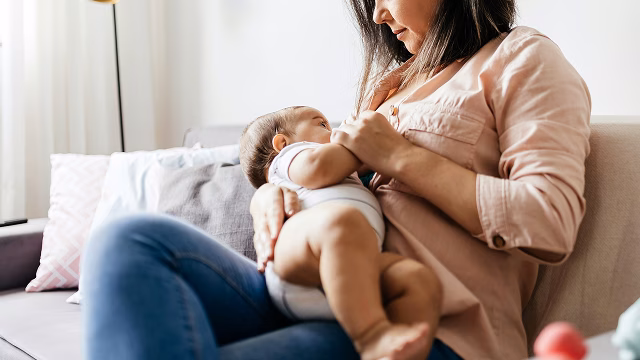 Woman in jeans and pink top breastfeeding a baby