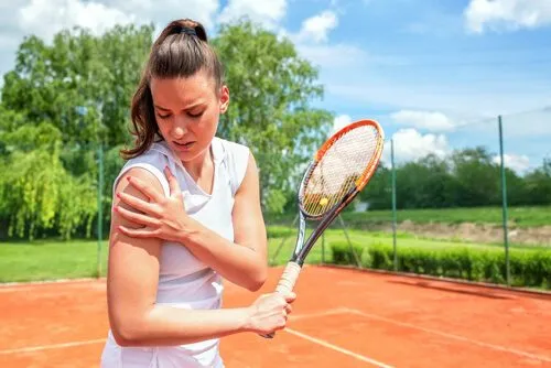 Tennis player holding her painful shoulder on a clay court