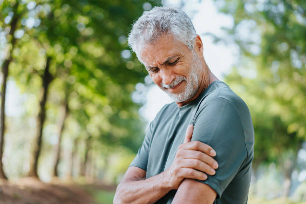 Older man outdoors holding his shoulder and experiencing shoulder pain.