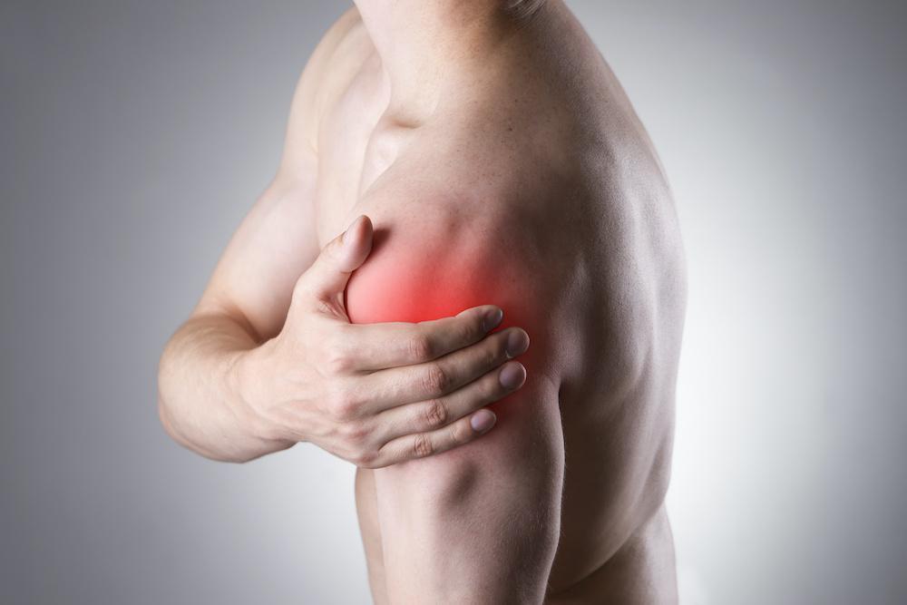 Person experiencing shoulder pain and holding the affected shoulder