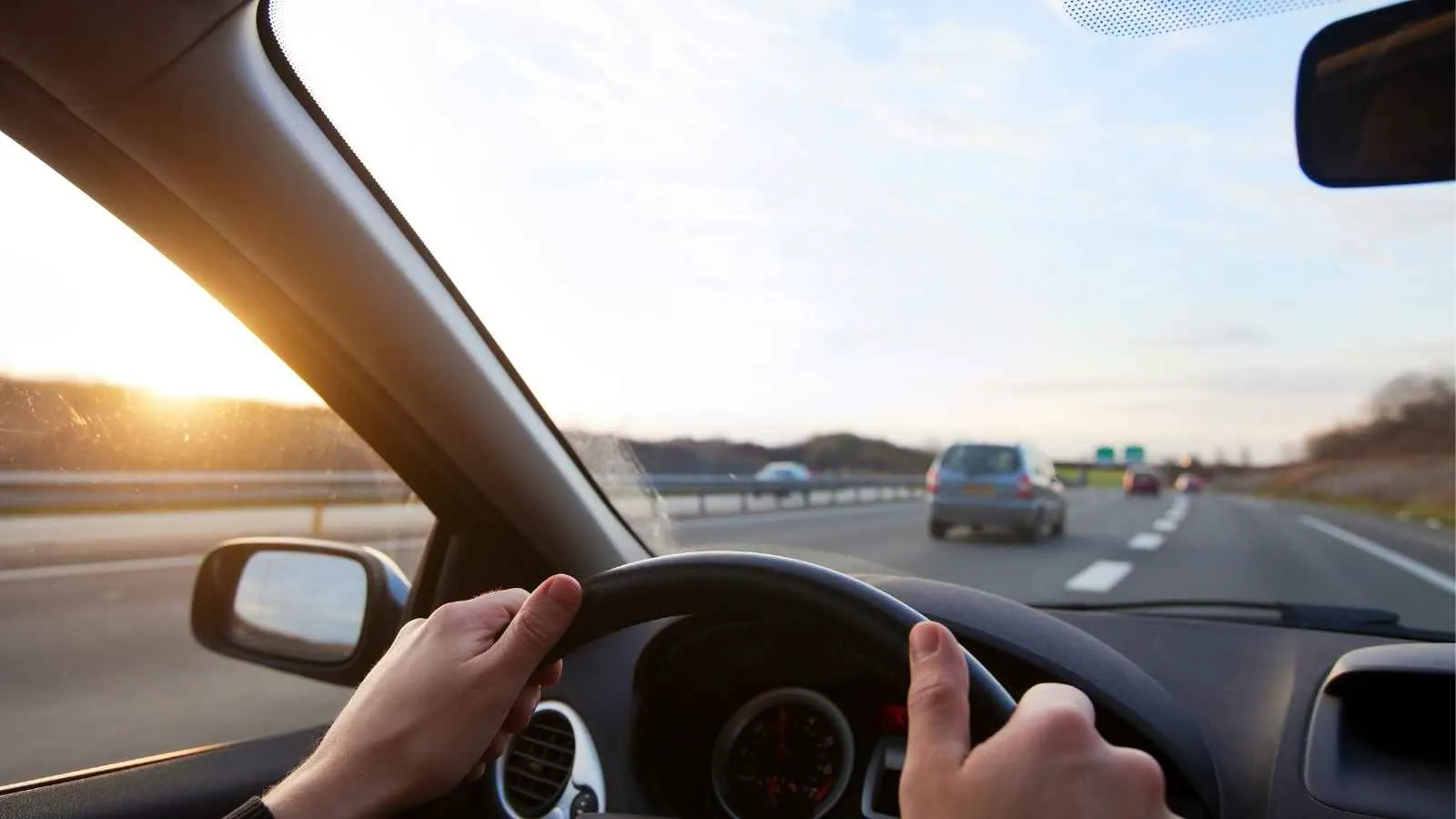 Person driving a car on a highway at sunset.