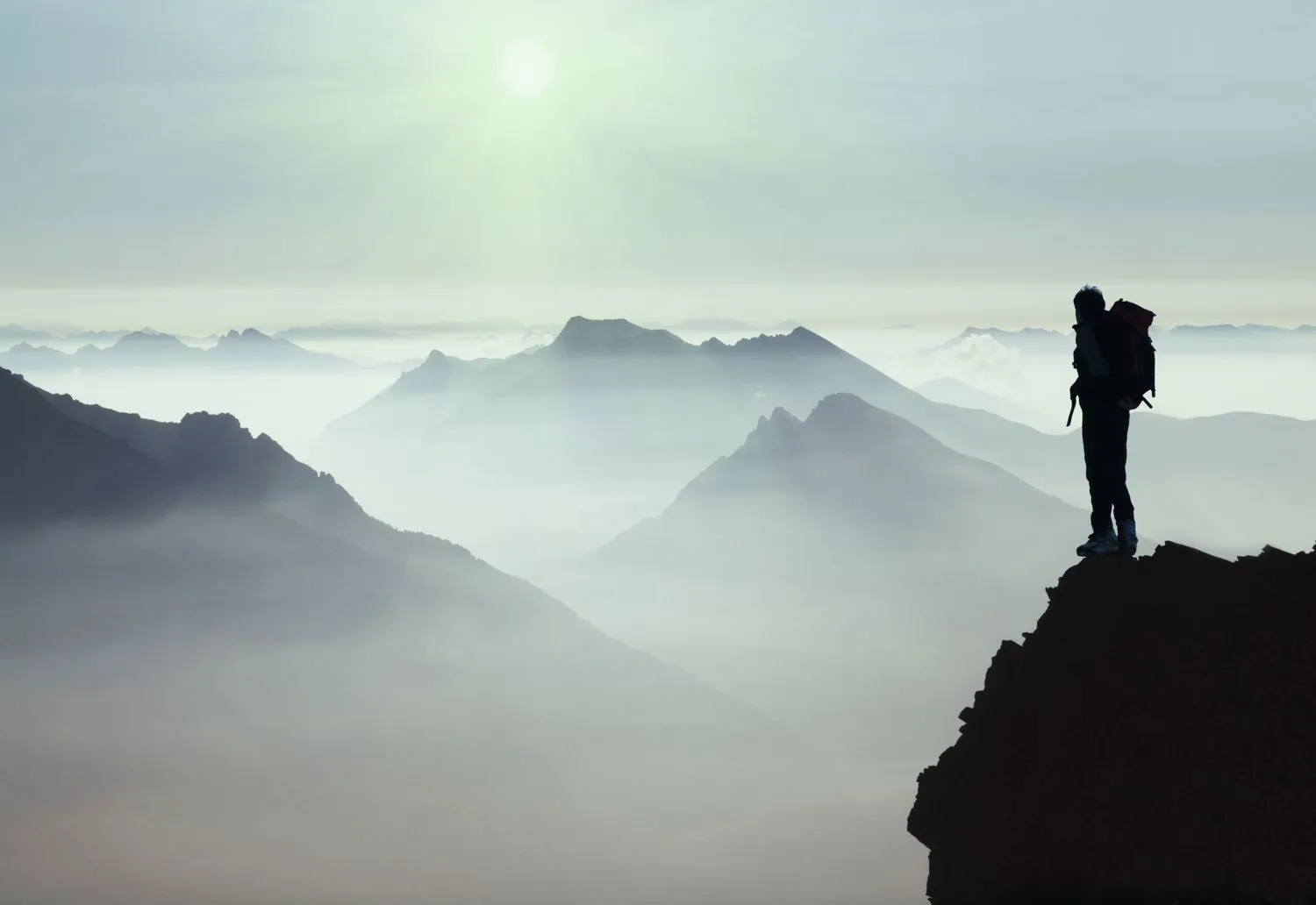 Hiker standing on a mountain ridge overlooking misty mountain peaks at sunrise.