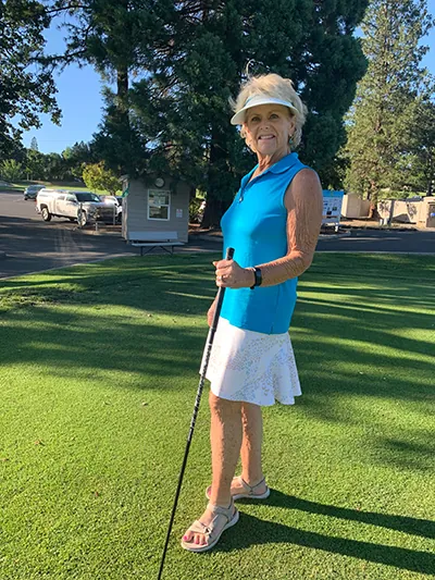 Woman standing on a golf course holding a golf club and posing after returning to golf.