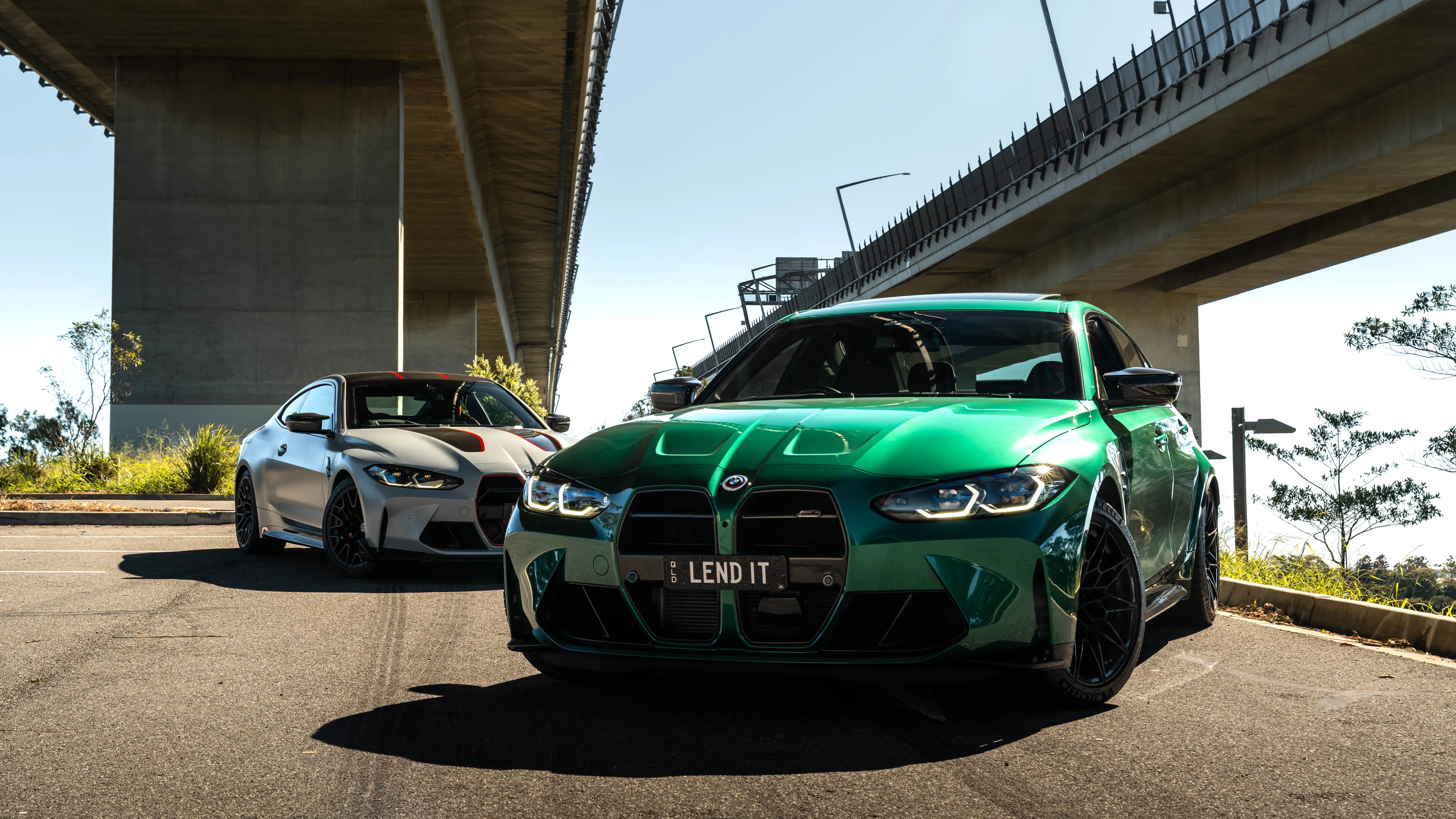 Two BMW M cars with LEND IT number plates parked under a motorway bridge