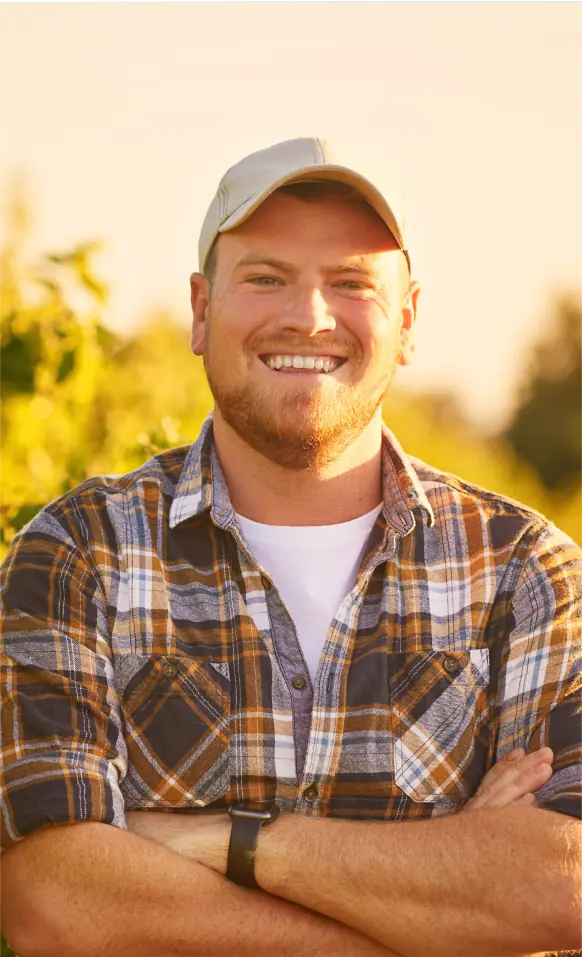 A man in a plaid shirt and cap smiles at the camera.