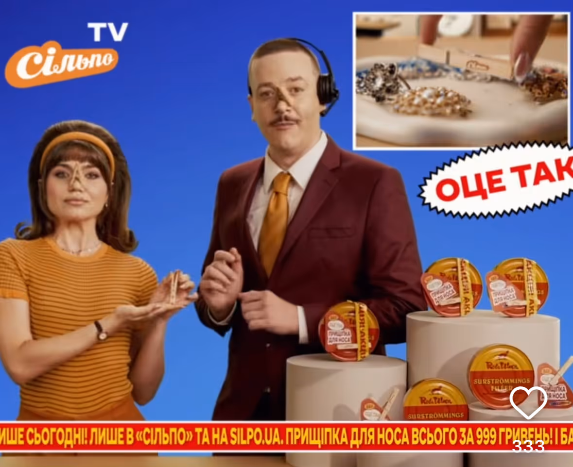 Two presenters, a woman in an orange striped shirt and a man in a maroon suit with an orange tie and headset, display nose clips against a blue background with multiple nose clip products on round white pedestals and a close-up inset of a hand picking a nose clip.