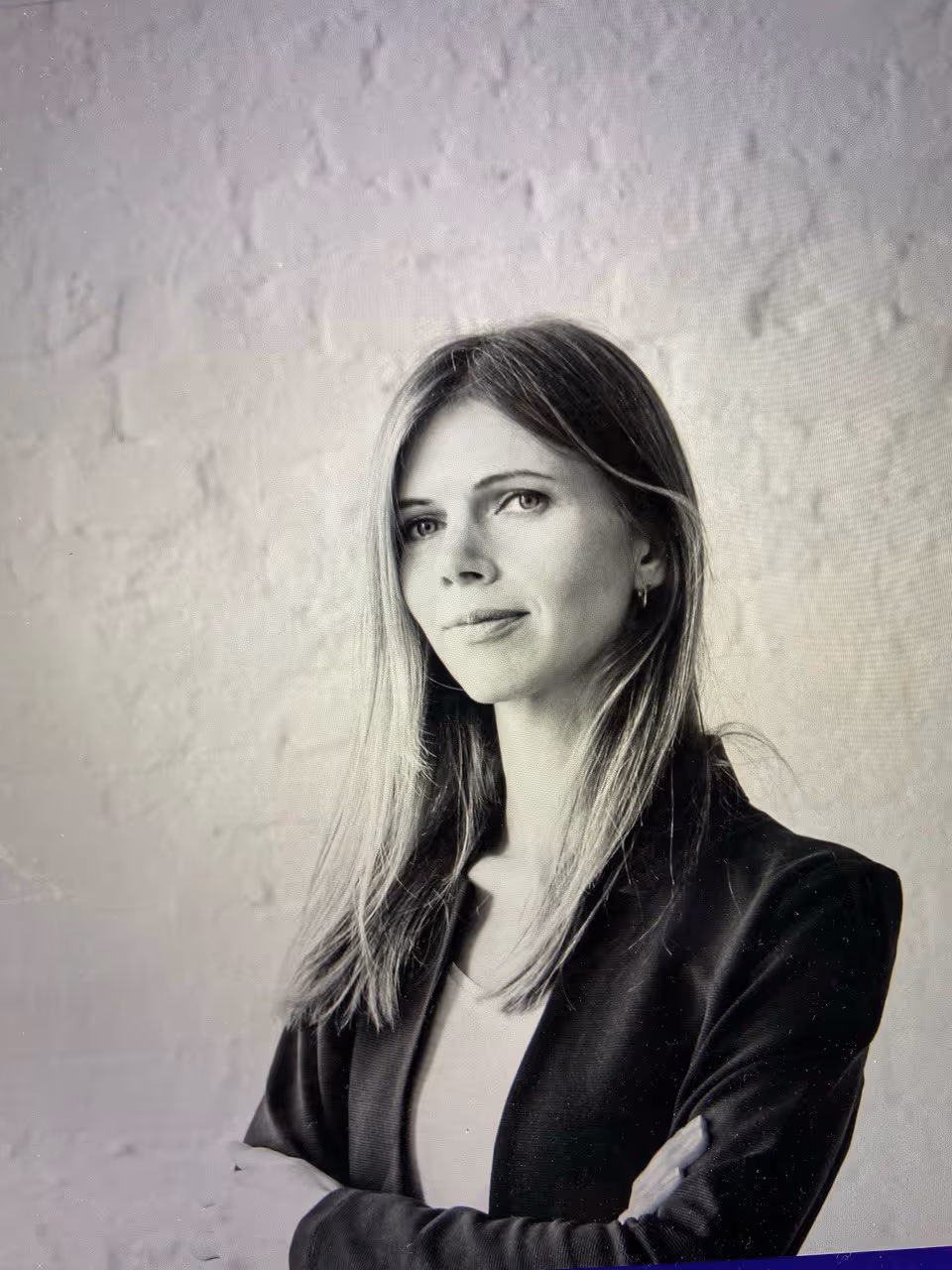 Black and white portrait of a confident woman with long hair wearing a blazer, standing with arms crossed.