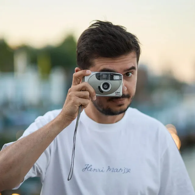 Portrait of a man with a mustache wearing a yellow shirt against a blue curtain background.