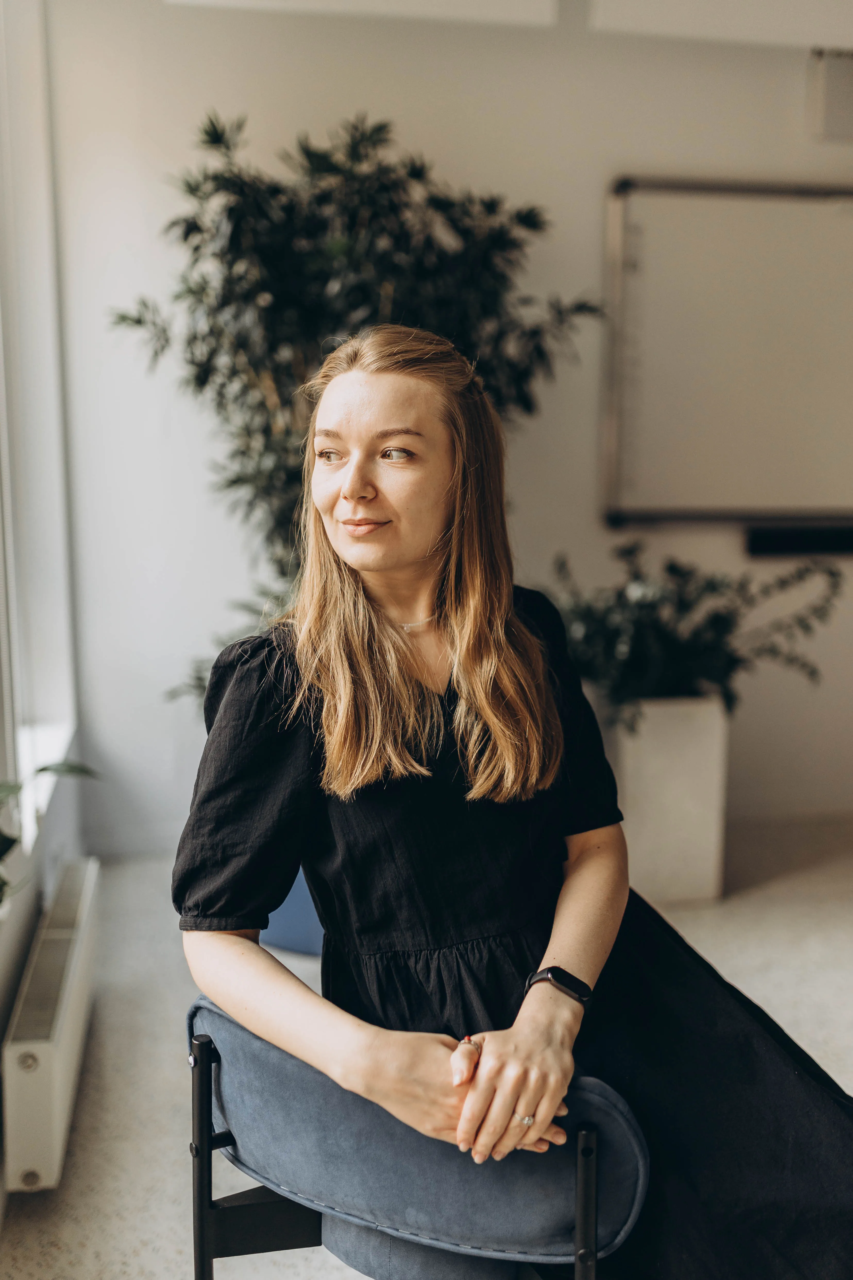 Smiling young woman with long hair sitting backwards on a chair in a bright room.