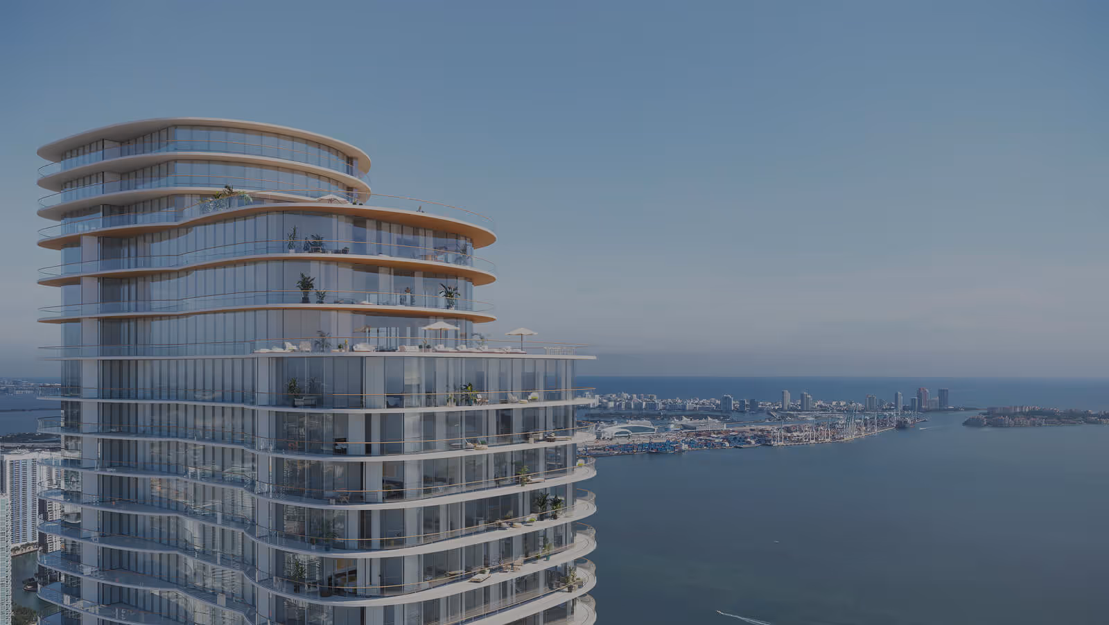 Modern curved glass high-rise building with balconies overlooking a calm harbor and city skyline under a clear blue sky.