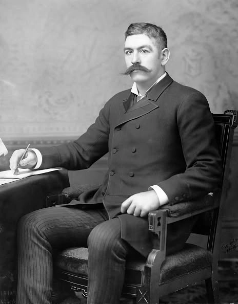 John L. Sullivan seated at a desk in a dark suit