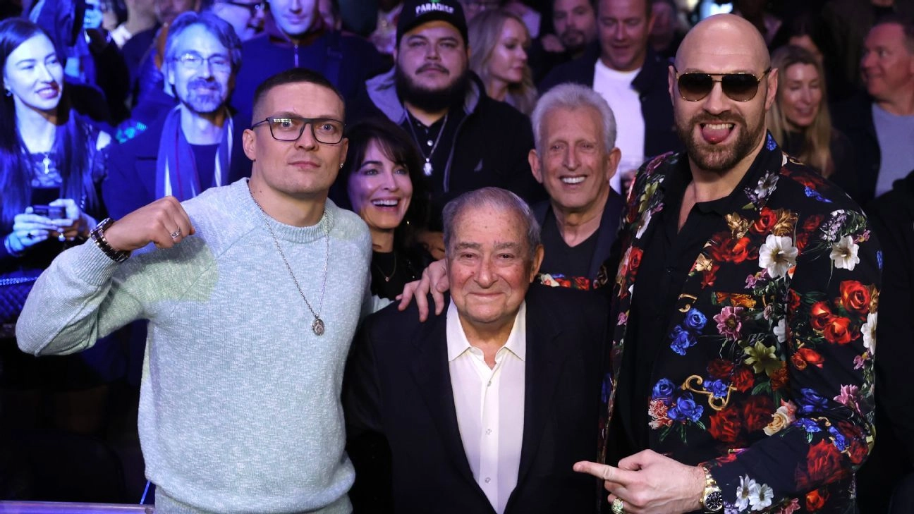 Oleksandr Usyk and Tyson Fury pose with Bob Arum in front of a crowd.