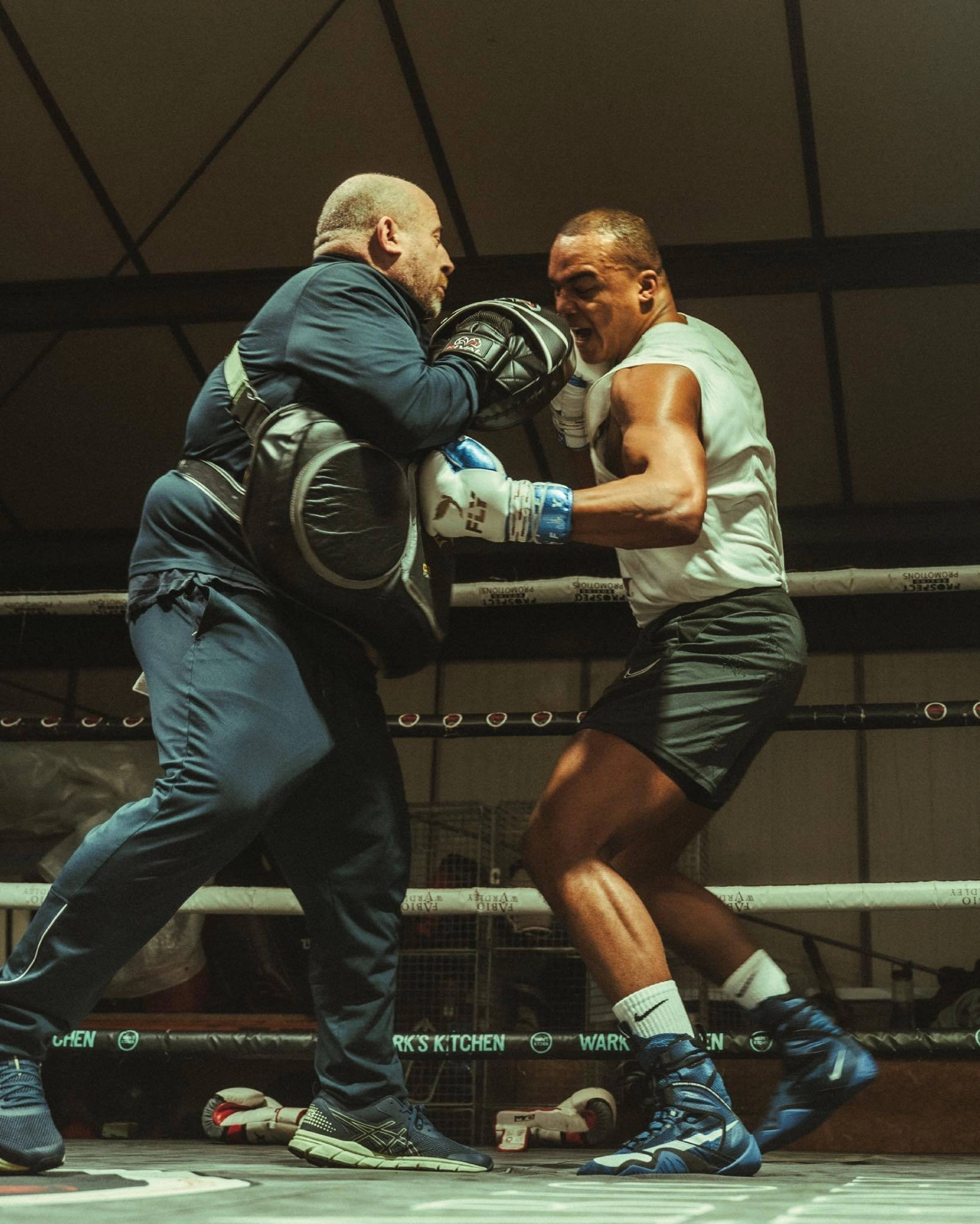 Fabio Wardley in a white shirt and boxing gloves works on close-range punches with a trainer wearing a body protector and focus mitts.