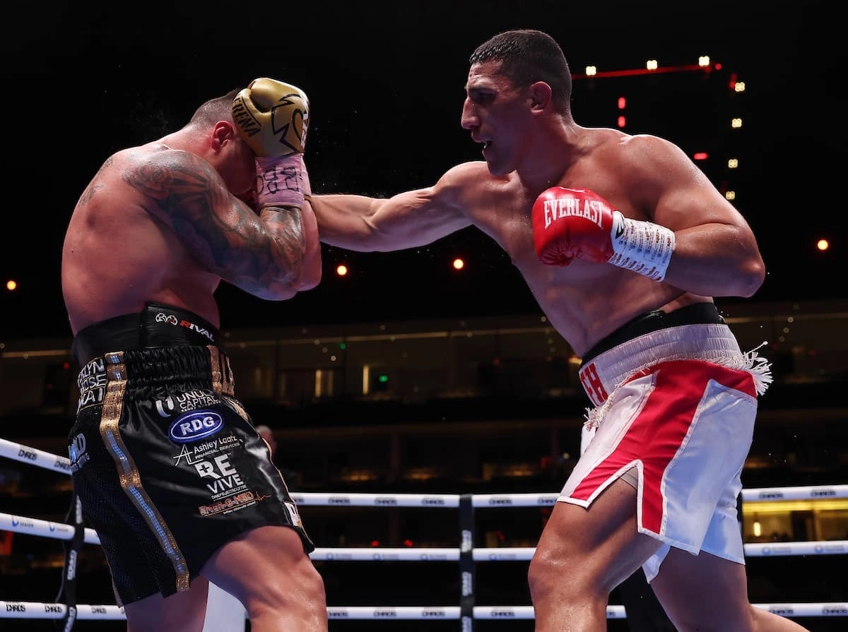 Justis Huni on the right extending a punch toward Kevin Lerena, who covers his head with gold gloves near the ropes.
