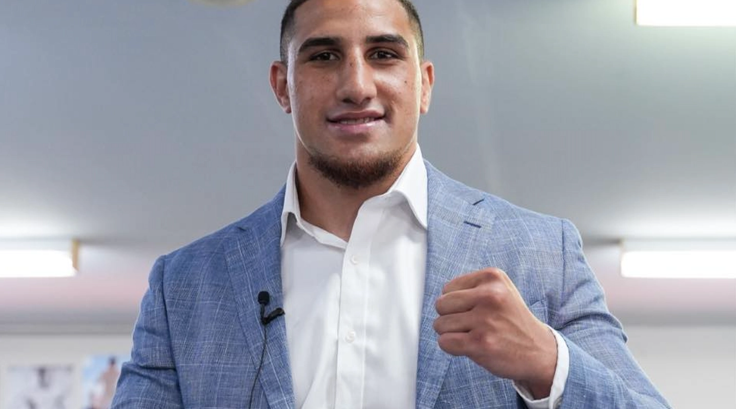 Justis Huni wearing a light blue jacket and white shirt while raising a fist.