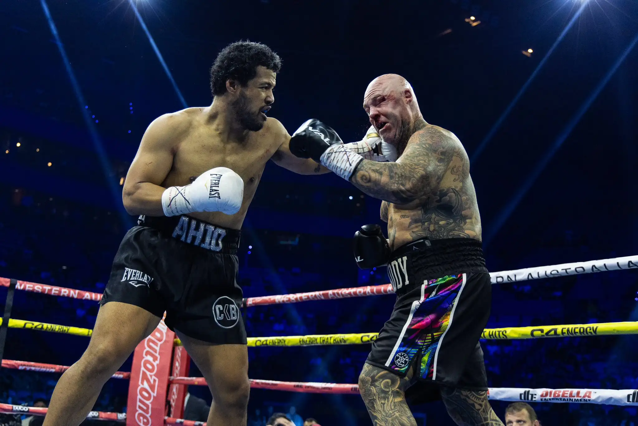 Hemi Ahio punching Lucas Browne near the ropes, with Ahio wearing white gloves and Browne black gloves.
