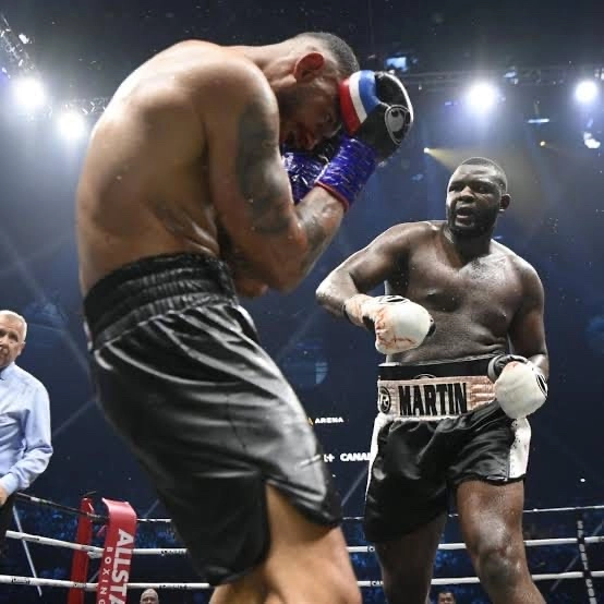 Martin Bakole in black trunks facing an opponent covering his head near the ropes.