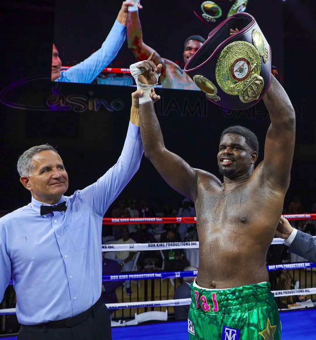 Cassius Chaney raising a championship belt as the referee lifts his other arm.