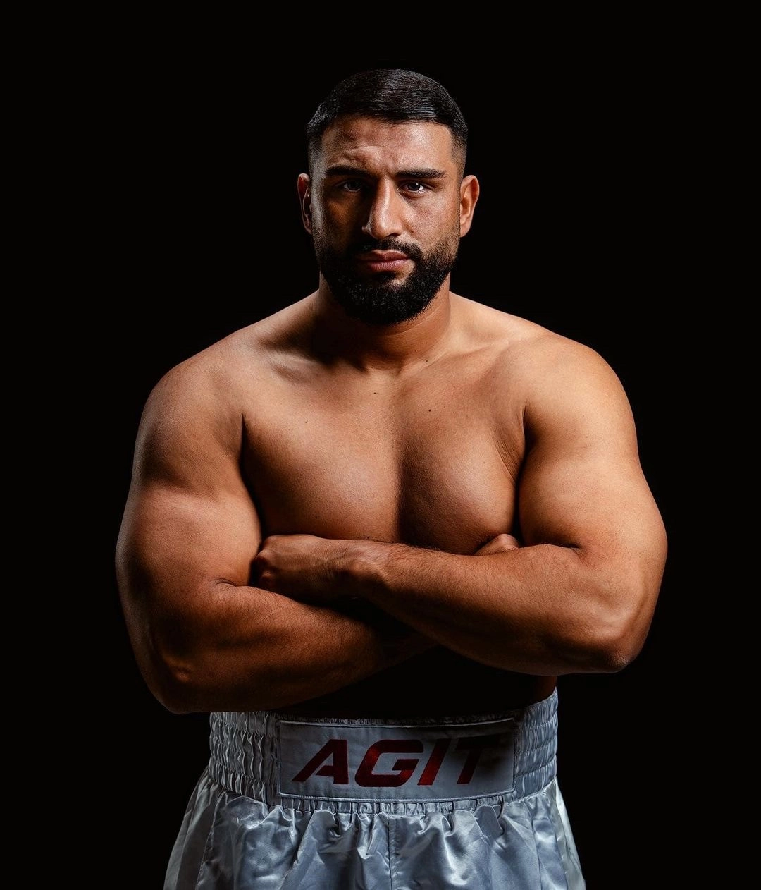 Agit Kabayel with arms folded in silver trunks bearing Agit lettering against a black background.