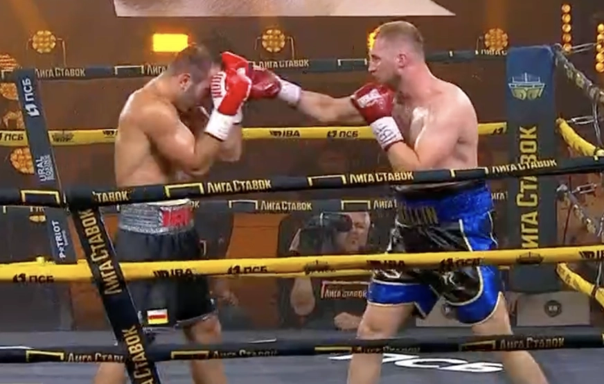 Two heavyweights in red gloves boxing, with the fighter in blue trunks extending a punch toward his opponent’s raised guard.