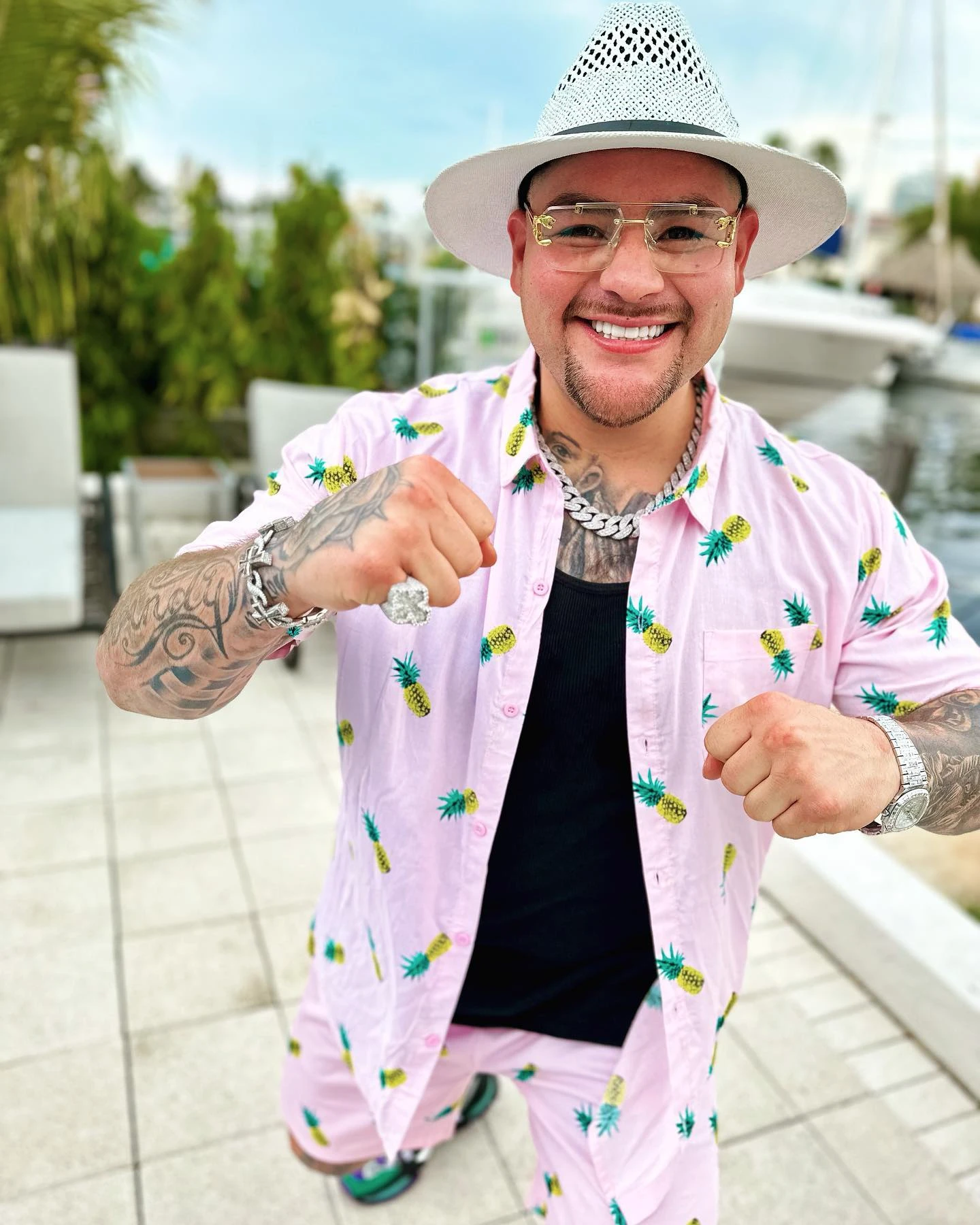 Andy Ruiz Jr smiling with raised fists, wearing a white hat, glasses and a pink pineapple-patterned shirt and shorts.
