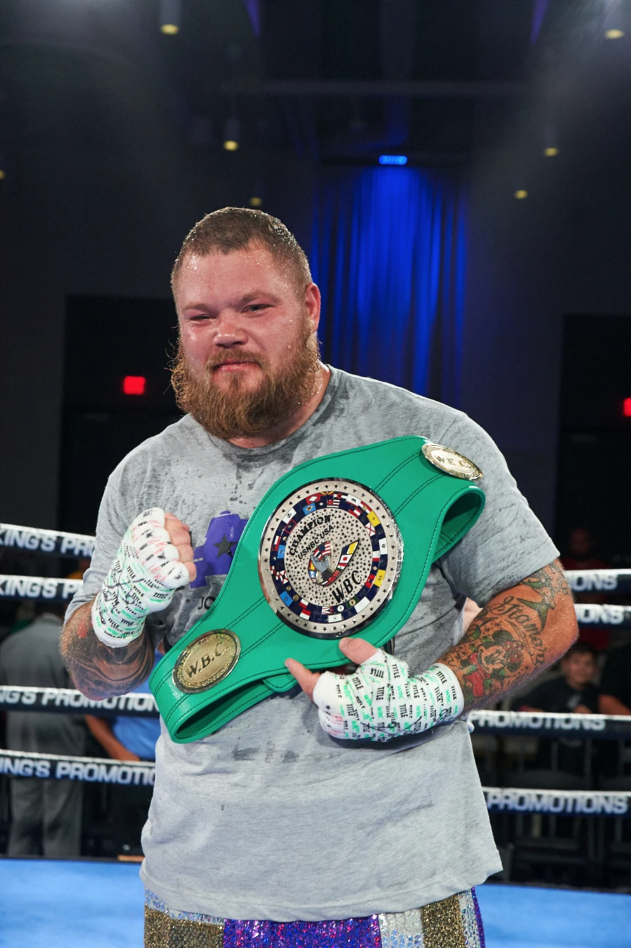 Joey Dawejko in a grey shirt holding a green WBC belt across his chest with a wrapped fist raised.