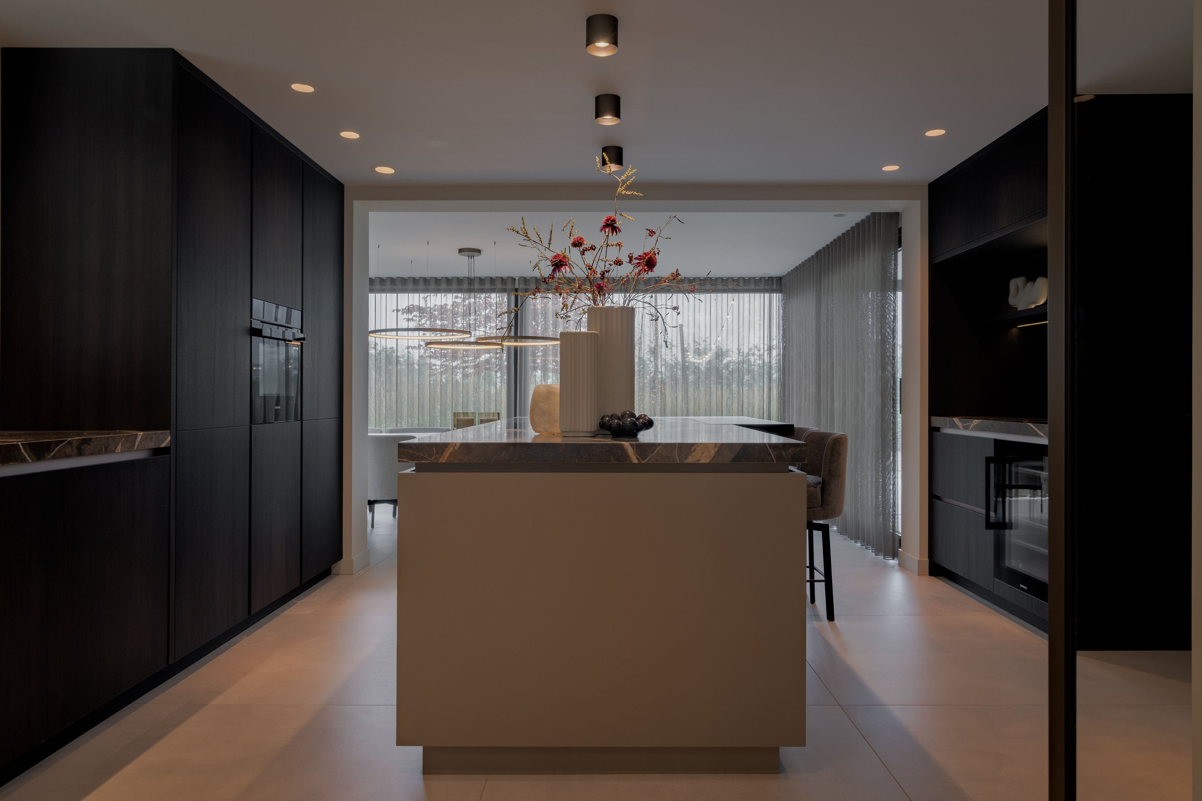 Luxe maatwerk keuken met kookeiland, donkere kastenwand en natuurstenen werkblad