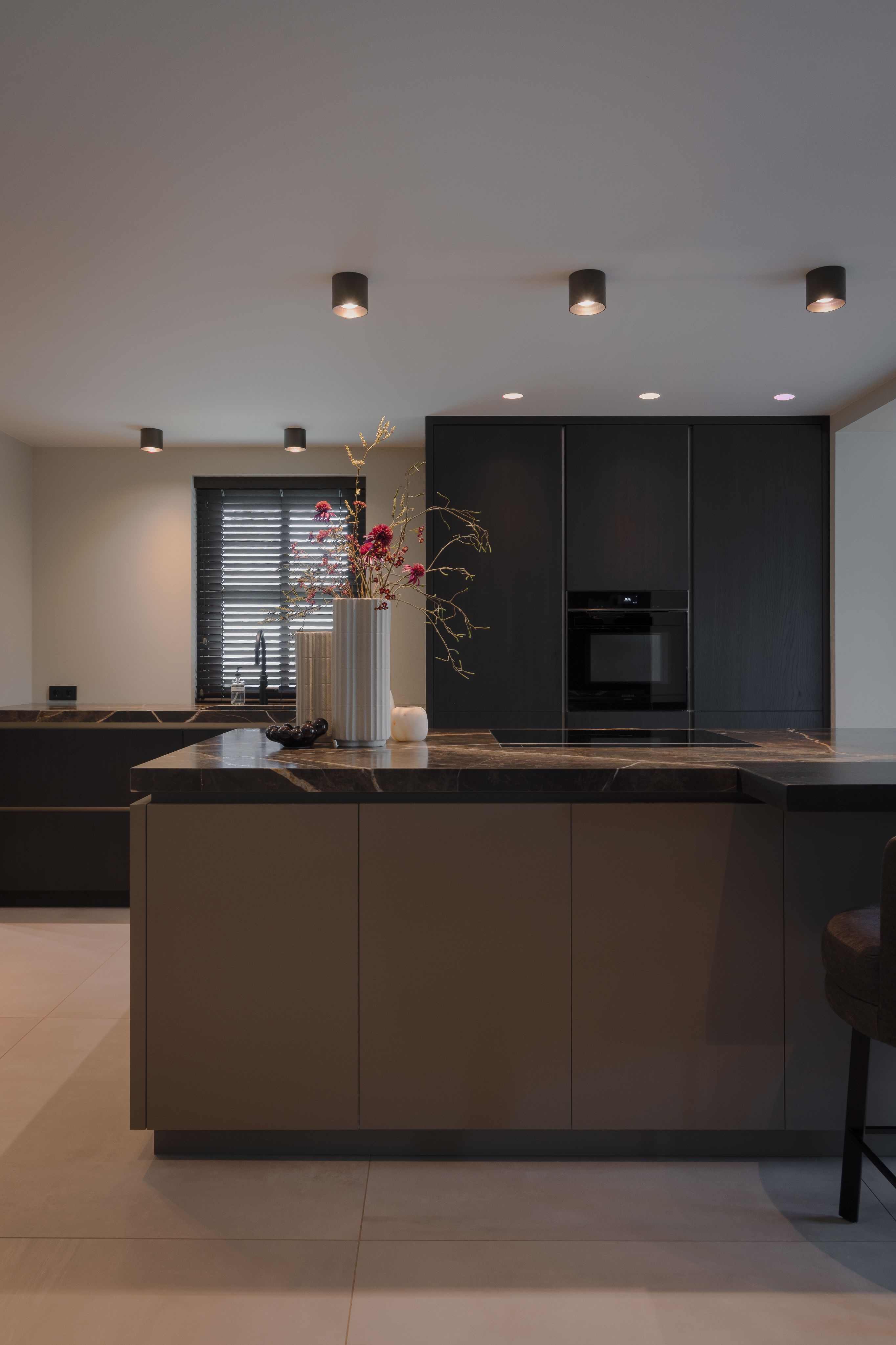 Luxe keukeneiland met natuurstenen werkblad en donkere maatwerk kastenwand