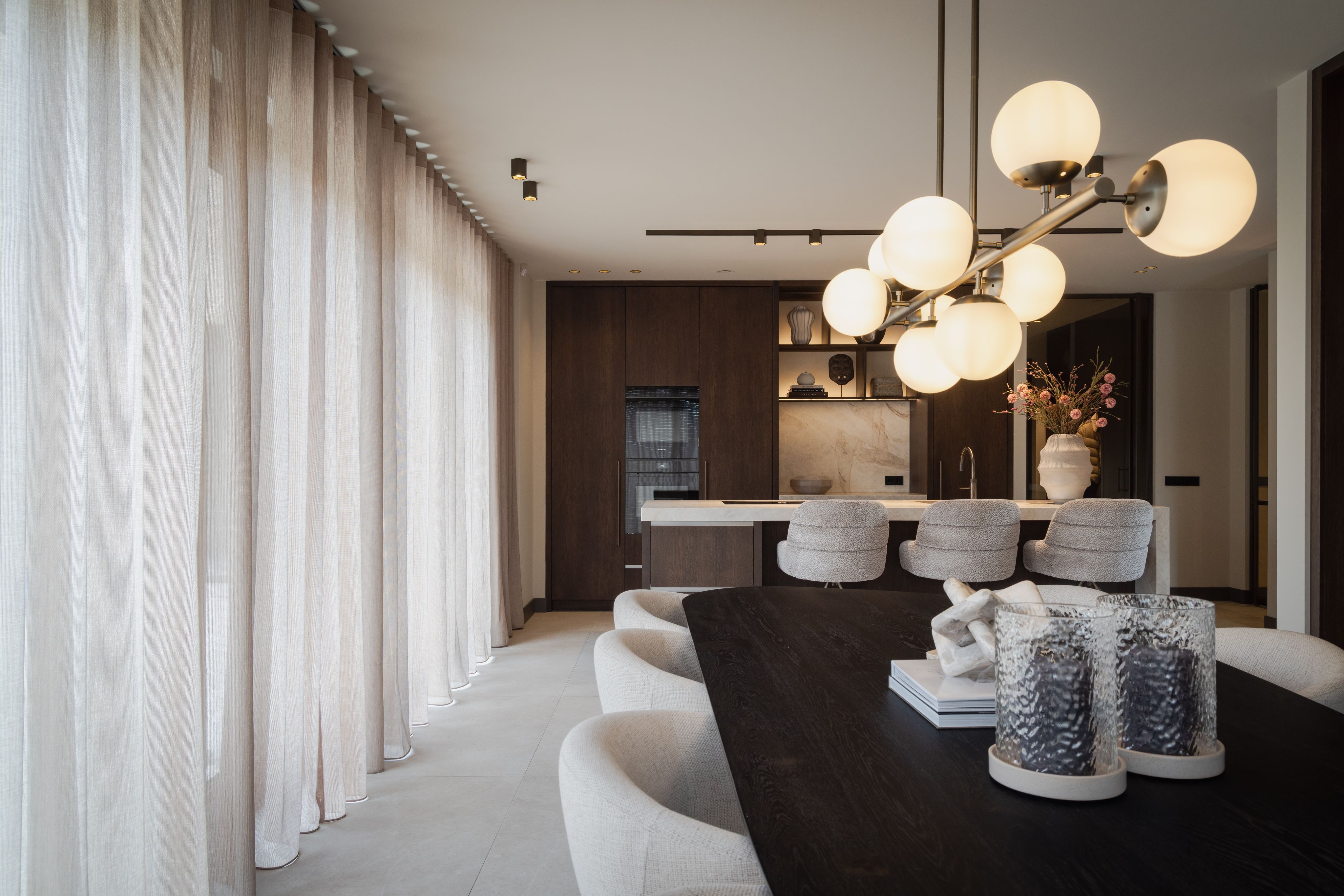 Open keuken en eetkamer met donkere eettafel en lichte gestoffeerde eetkamerstoelen