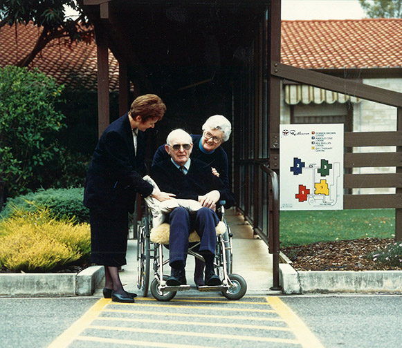 Client sitting on wheelchair with two ladies around him looking at the camera