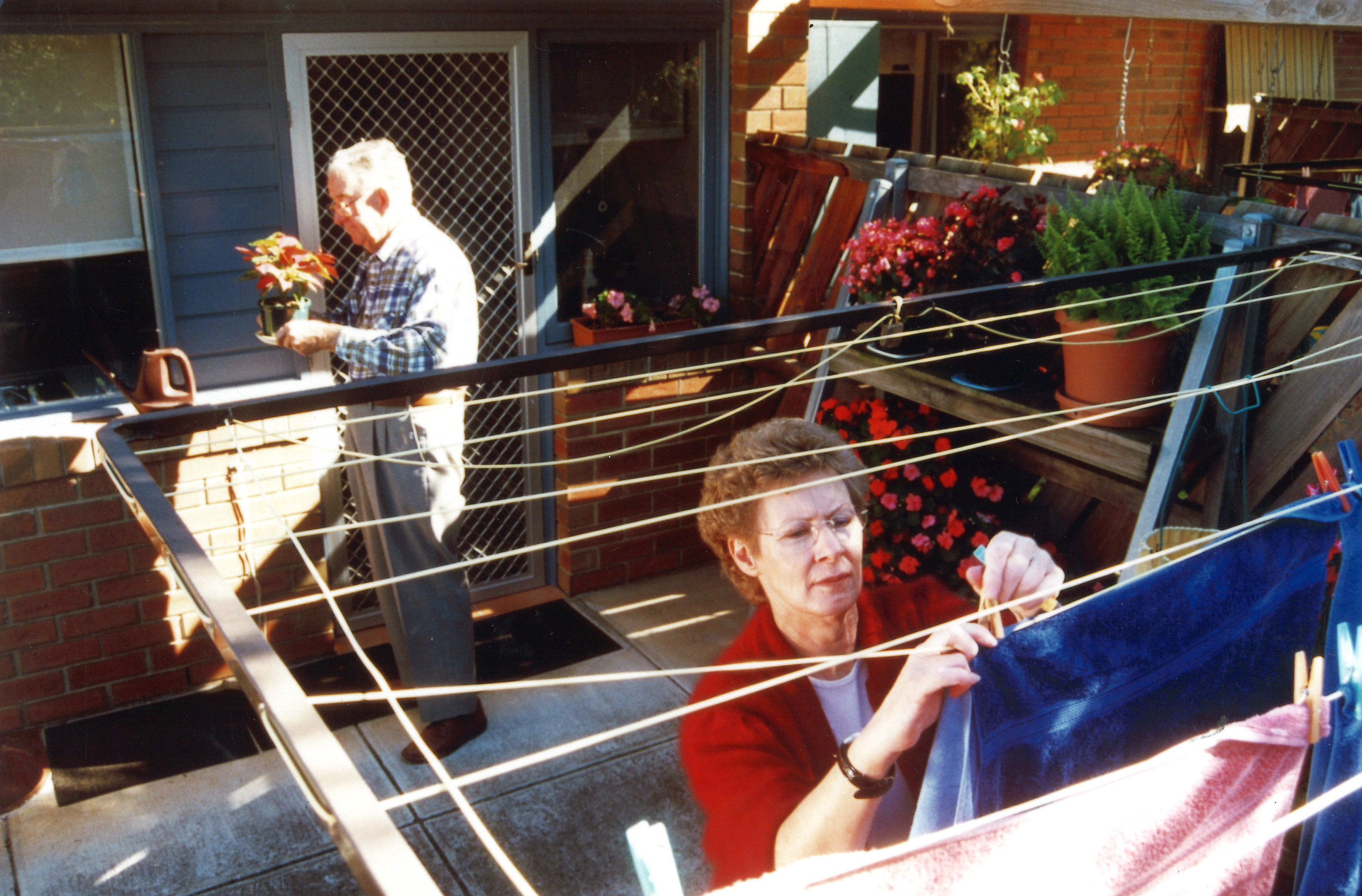 Lady hanging clothes on clothes hanger with man holding a plant pot behind her