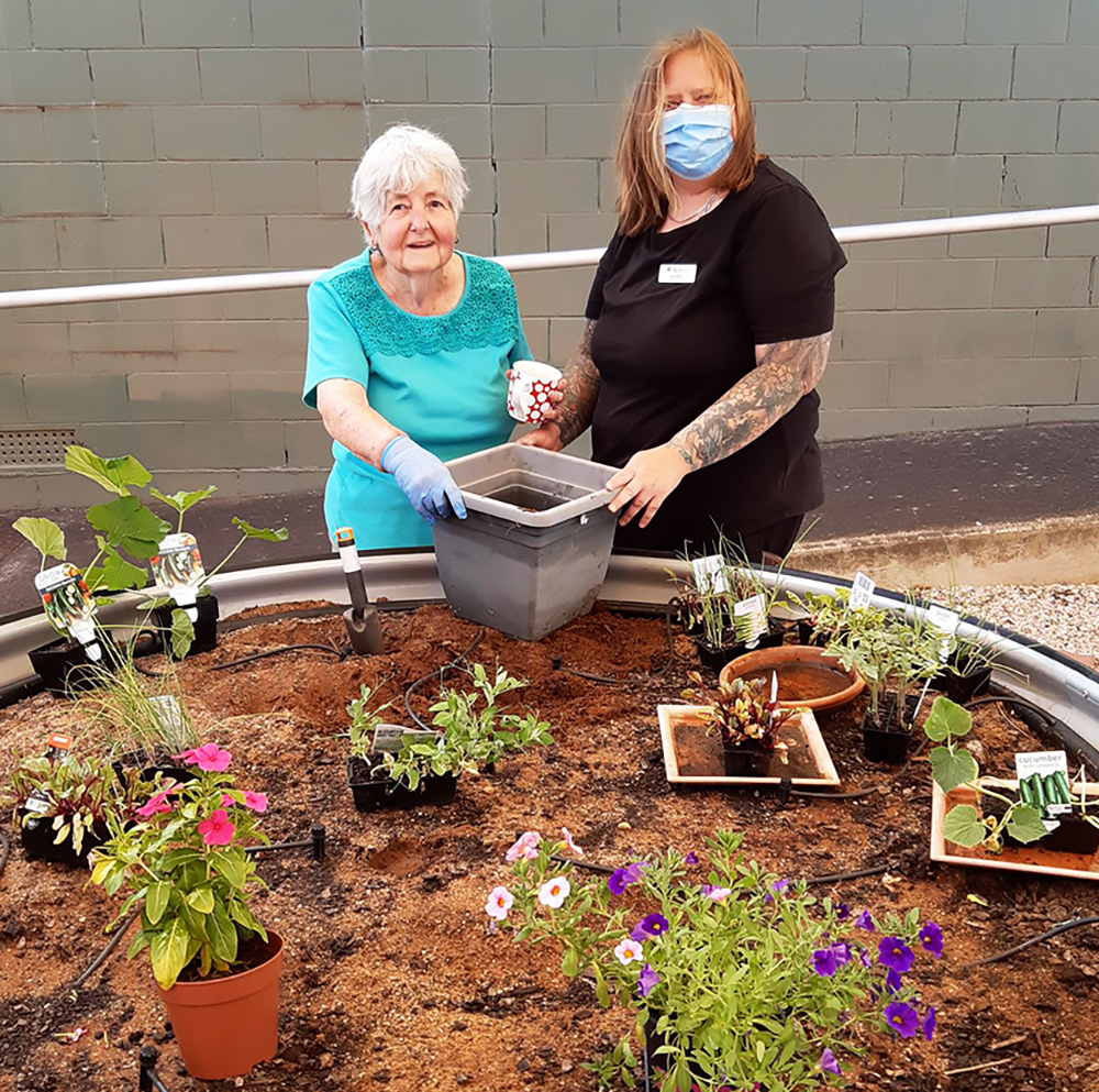 Older lady with helper wearing mask holding a pot