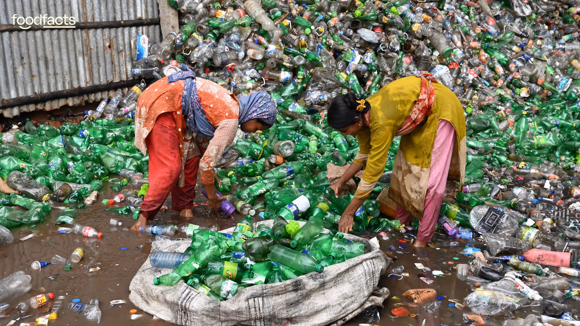 A beach heavily littered with plastic waste, including bottles, containers, and other debris, stretches alongside a scenic shoreline with lush green cliffs and calm ocean waves. The image, featured in a FoodFacts.org article, emphasizes the environmental toll of food packaging and highlights the urgent need for sustainable alternatives to reduce plastic pollution in marine ecosystems.