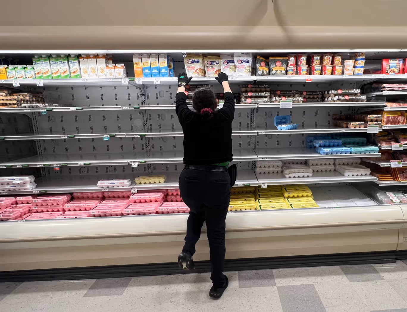 A grocery store worker rearranges items in the depleted egg section