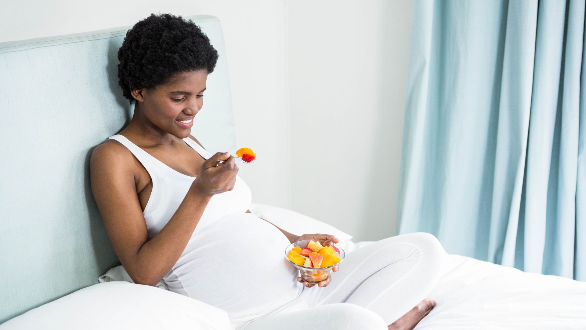 A pregnant women is eating a bowl of fruit
