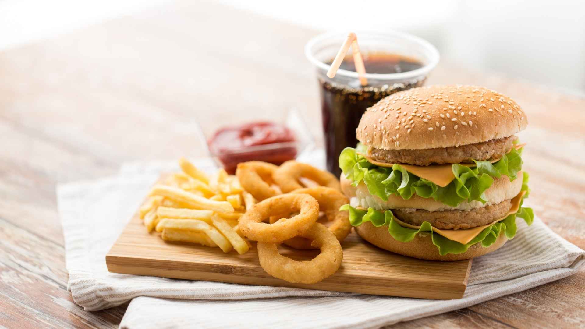 A typical fast food meal of a burger, onion rings, potato chips, and cola