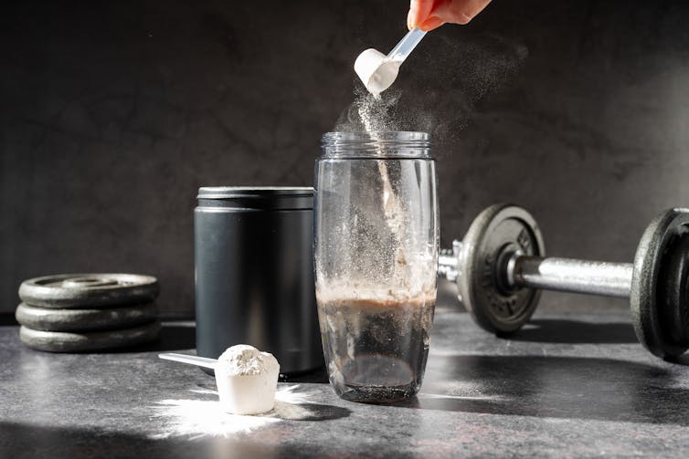 A person dumps a scoop of creatine powder into a cup.